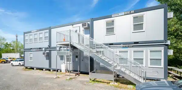 Double-story modular building with external staircase under a clear blue sky.