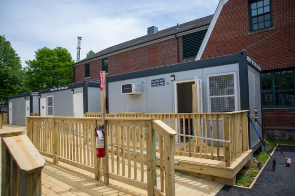 Portable buildings with wooden ramps outside a brick structure on a sunny day.