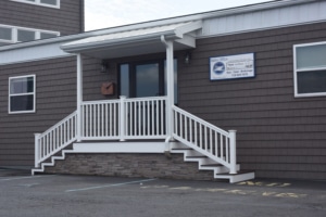 Office building entrance with brown siding and white railing steps, parking space in front