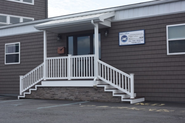 Office building entrance with brown siding and white railing steps, parking space in front