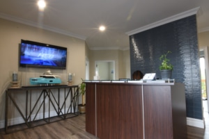 Modern reception area with wooden desk, sleek TV setup, and decorative plants, creating a welcoming atmosphere.