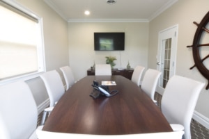 Modern conference room with wooden table, white chairs, and wall-mounted TV screen