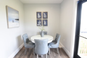 Cozy dining nook with grey chairs around a white round table and decorative wall art in a bright space.