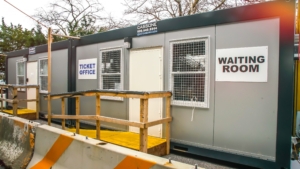 Portable ticket office and waiting room with ramp access surrounded by trees.