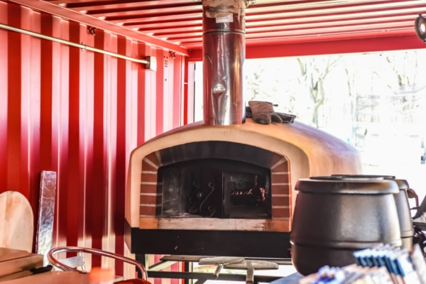 Wood-fired oven inside a red shipping container kitchen setup
